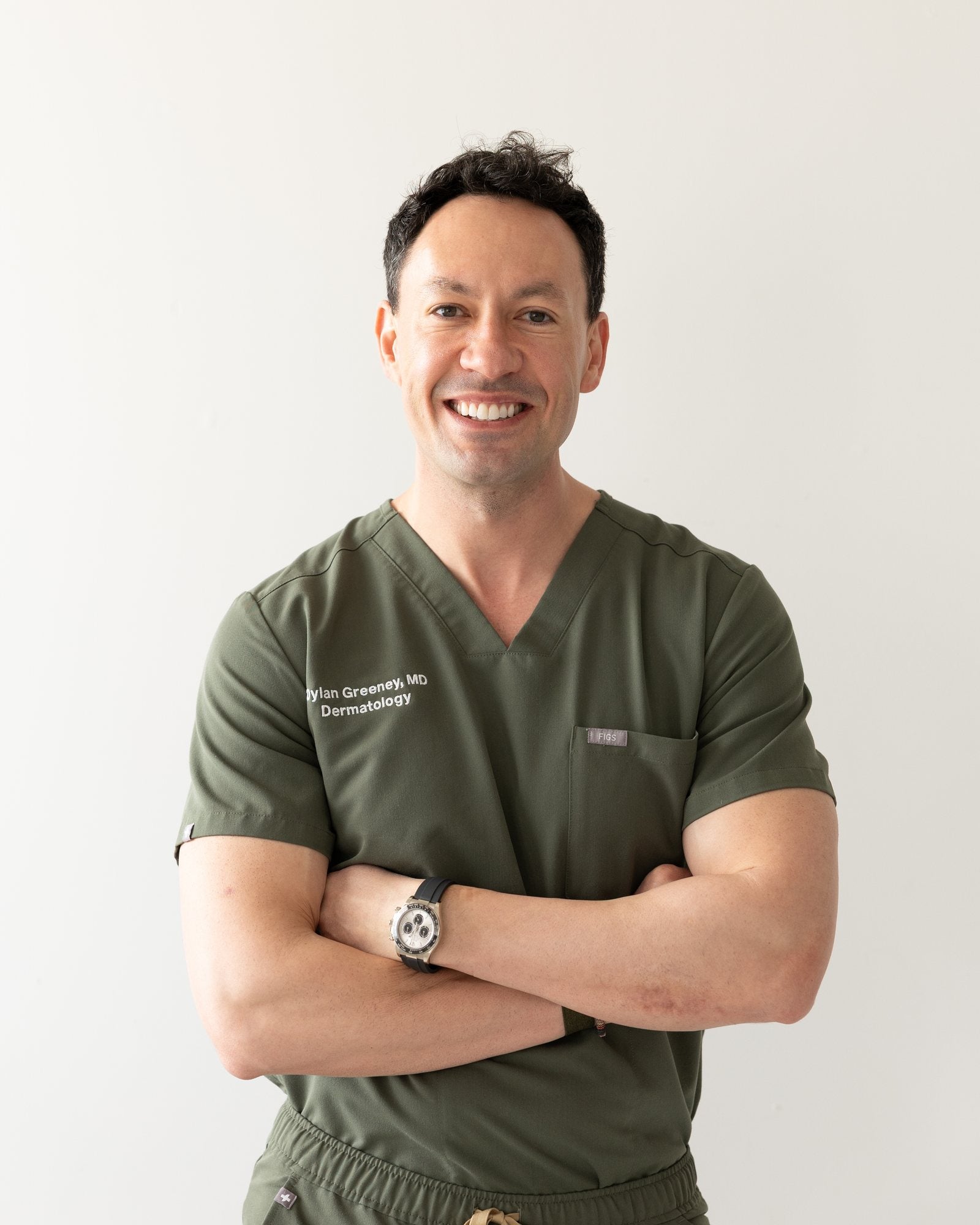 Dylan Greeney MD, FAAD, board-certified dermatologist wearing green medical scrubs